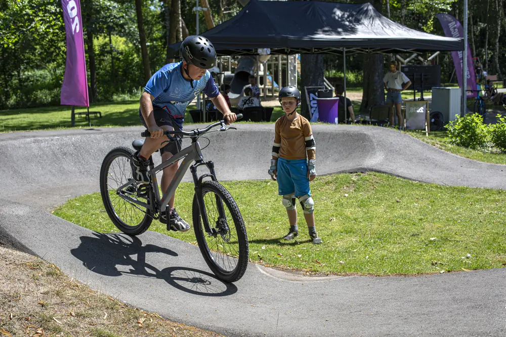 Nastolatek na rowerze pumptrackowym obok instruktora, w tle namiot strefy testów