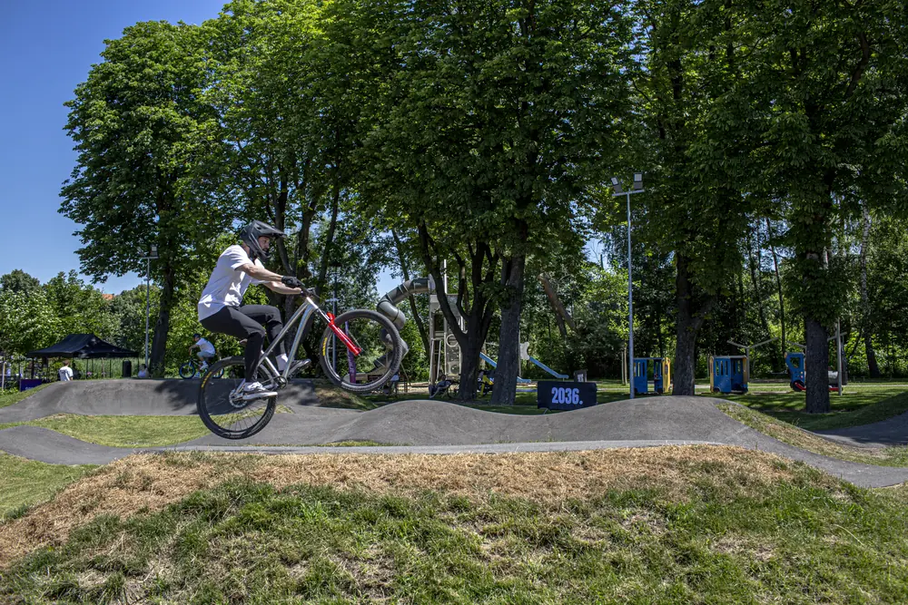 Instruktor skacze rowerem nad garbem pumptracka